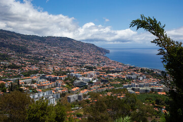 Panoramic view of Funchal, the capital of Madeira Island, showing the city sprawled along the hillside with the Atlantic Ocean in the background on a sunny summer day.