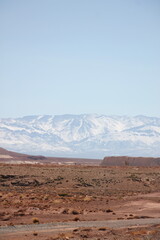 Mountains with snowy peak and a road that leads there with a blue sky and the sun shining