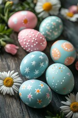 Fototapeta premium Colorfully decorated Easter eggs in pink and blue are arranged on a rustic wooden surface, accompanied by blooming daisies and other spring flowers
