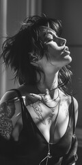 Black and white photo of an attractive woman with messy hair, wearing a necklace, looking up with eyes closed, sunlight and shadows on her face.