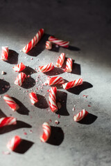 close-up of broken pieces of a red and white Christmas candy cane in shadows against a gray background 
