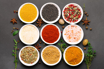 Bright set of aromatic organic spices and herbs such as smoked paprica, peppercorn, thyme, bay leaf, curry, dry garlic and others on black stone background top view.