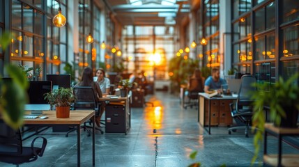 A modern office space with people working amid plants and warm sunset lighting.