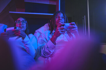 Happy young latin couple sitting on the sofa in the living room, having fun playing video games together at home. Concept Gaming streaming