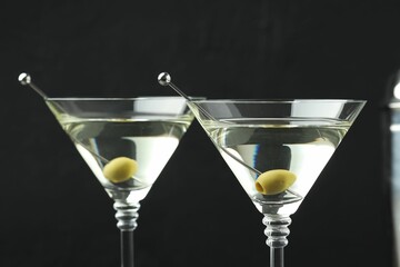 Martini cocktail with olives in glasses on black background, closeup