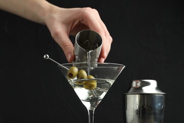 Woman making martini cocktail with olives on black background, closeup