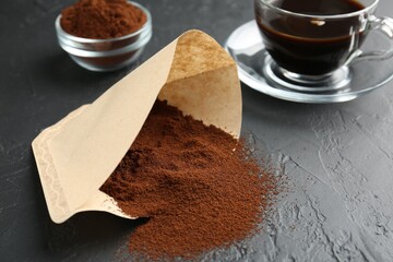 Paper filter, ground coffee and cup of drink on black table, closeup