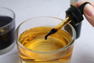Iodine starch test. Woman dripping iodine into glass of water at white table, closeup