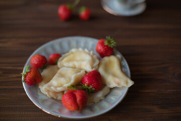A close-up of a plate of homemade dumplings with fresh strawberries, lightly dusted with powdered sugar, placed on a dark wooden table. The warm tones create an inviting and cozy atmosphere.