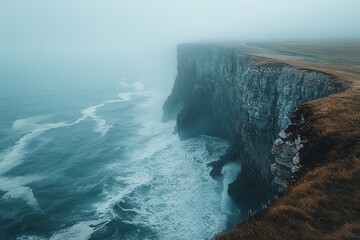 Foggy cliffs and waves crashing against rocky shore at dawn along a coastal landscape in the early...