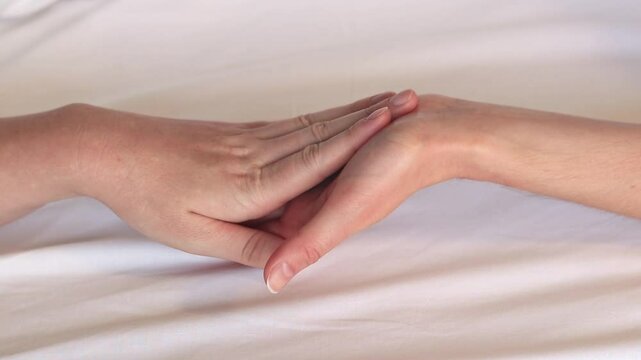 Same-sex relationships, lesbians. Same-sex marriage and love concept. Happy lesbian couple. Two female hands touching each other against white sheets. Two female hands in bed close-up. LGBTQ
