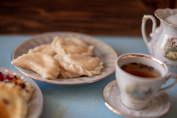 A plate of sweet dumplings with strawberries on a light blue table, with a bite taken out to reveal the creamy filling. A cup of tea sits nearby, completing the relaxing scene.
