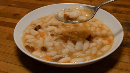 A white plate with traditional baked white beans and a full spoon ready to eat. Mediterranean diet