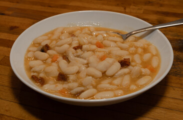A white plate with traditional baked white beans and a full spoon ready to eat. Rioja traditional food (Spain)
