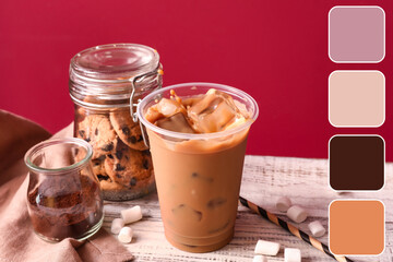 Plastic cup of delicious iced coffee with splashes and jar of cookies on table