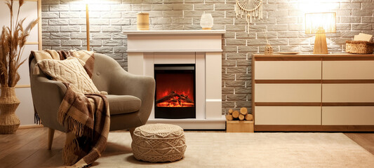 Fototapeta premium Interior of stylish cozy living room with fireplace, armchair and glowing lamps in evening