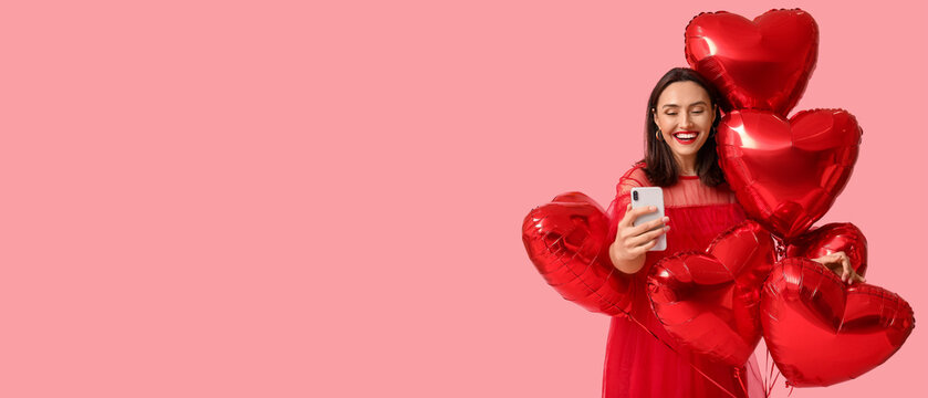 Happy young woman with mobile phone and heart-shaped air balloons on pink background. Online dating