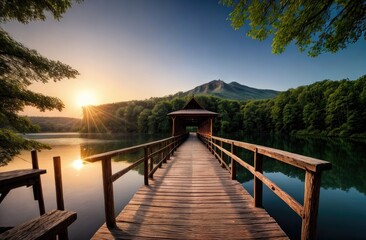 Fototapeta premium A peaceful wooden pier leads to a covered structure over a reflective lake, surrounded by lush green forest and mountains at sunrise, with golden sunlight casting serene reflection