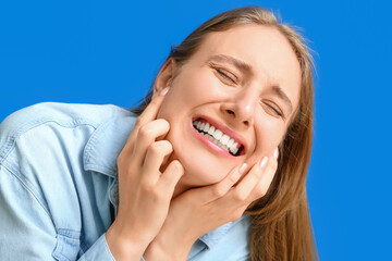 Emotional young woman suffering from toothache on blue background