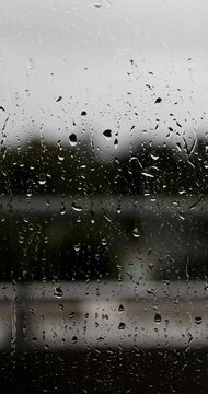 Portrait footage of rain drops rolling down a window on a hotel balcony, on a cloudy rainy bad wether day