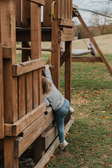 Young child climbing on a wooden outdoor play structure in a grassy park, showcasing adventurous playtime and childhood exploration in a natural setting with wooden playground equipment
