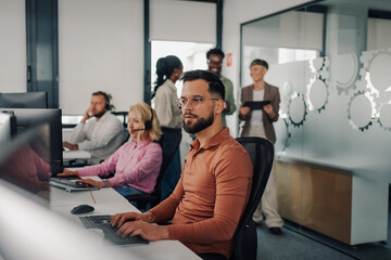 Focused male operator working on computer in busy call center