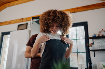 Man helping woman putting apron on in kitchen