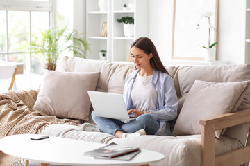 Beautiful young happy woman with laptop sitting on sofa at home