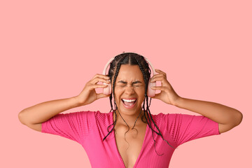 Fototapeta premium Emotional African-American woman listening to music on pink background