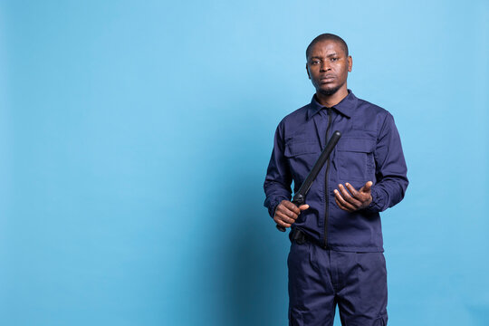Security agent presenting his baton weapon while on duty, working on protecting and safeguarding the perimeter. Professional armed guard with huge responsibility poses against blue background.