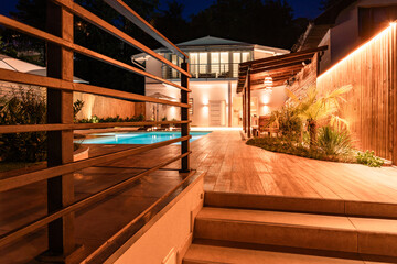 Luxury villa with lit staircase leading to swimming pool at night. Concept of outdoor modern home...