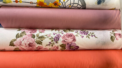 A colorful assortment of fabric rolls featuring floral patterns, solid tones, and intricate designs. Perfect for sewing projects, home decor, or creative crafting.