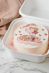 Little birthday bento cake in a gift box decorated with cute pink cream rabbit holding heart shaped balloons painting. Cake for a one month old girl on the white marble background