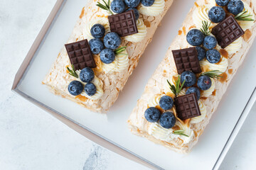 Homemade meringue roll decorated with almond flakes, blueberries and mini chocolate bars in the white gift box on the white background. Meringue roulade with whipped cream on top.
