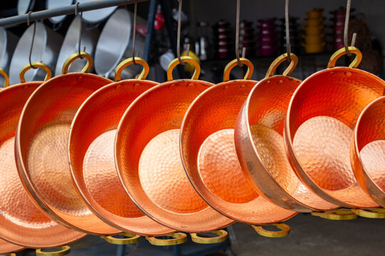 Alguns tachos grandes de cobre, muito polidos, pendurados, em exposi&ccedil;&atilde;o para venda.