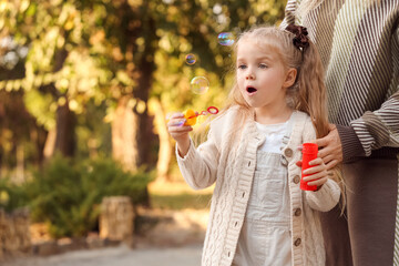 Little girl with her mother blowing soap bubbles in park on autumn day