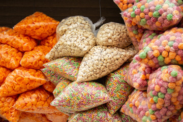 Alguns sacos plásticos com lanches industrializados;  salgadinhos, pipocas doce, cereais matinais, pendurados em exposição para venda em um comércio local.