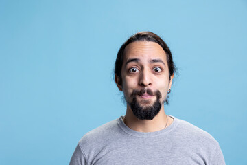 Obraz premium Male model with long curly hair posing with confidence in studio, standing with his casual wear against blue background. Young peaceful confident man with self assured attitude.