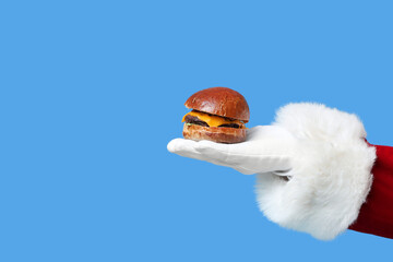 Hand of Santa Claus with tasty burger  on blue background