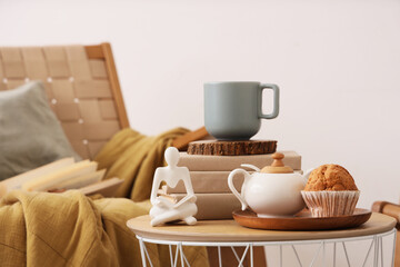 Coffee table with teapot, cup of tea, books and cake in living room. Closeup