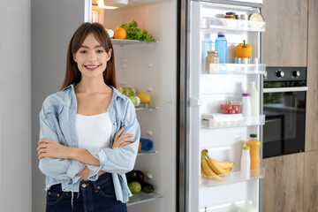 Young woman near open fridge in kitchen