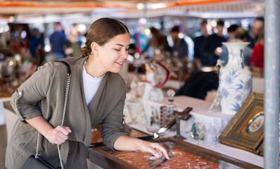 Portrait of glad smiling young woman choosing vintage goods at flea market