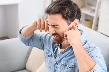 Young man with hearing problem covering his ears on sofa at home, closeup