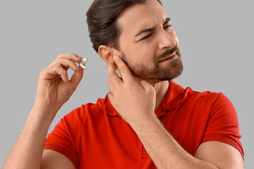 Young man with hearing problem holding earphone on light background, closeup