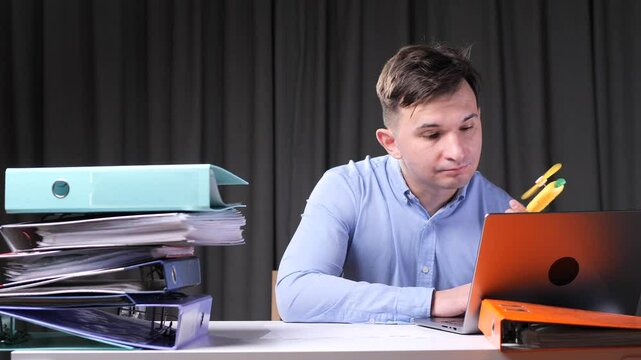 A man works on a laptop in the office and blows on himself with a hand fan