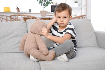 Little boy with toy bear suffering from ear pain on sofa at home