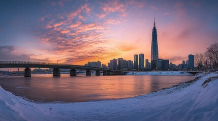 Panoramic sunset view of a city skyline with a river, bridge, and snow.