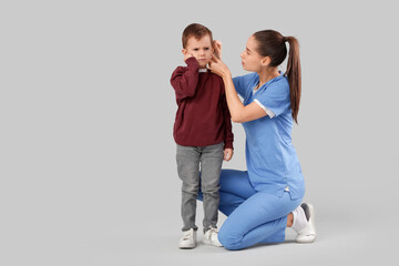 Female doctor examining little boy's ear with hearing problem on light background