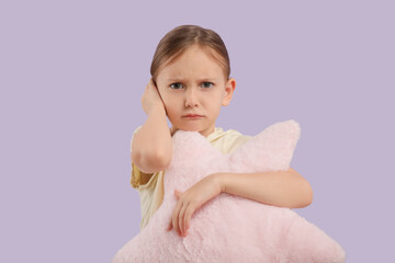 Little girl with pillow suffering from ear pain on lilac background