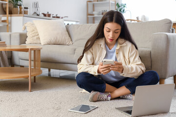 Beautiful young woman using mobile phone on carpet at home